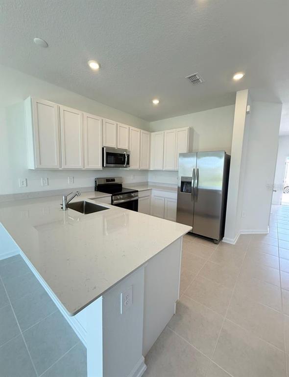 A modern kitchen features white cabinets, stainless steel appliances, and a large quartz-topped island — 2633 SKYLINE LOOP, KISSIMMEE, FL