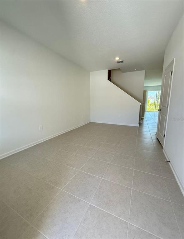 An empty room features light-colored tile flooring, white walls, and a staircase — 2633 SKYLINE LOOP, KISSIMMEE, FL