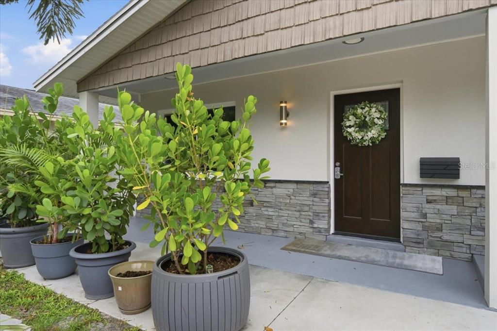 A front porch features potted plants, a dark wood door, and gray stone siding — 311 45TH AVENUE N, ST PETERSBURG, FL