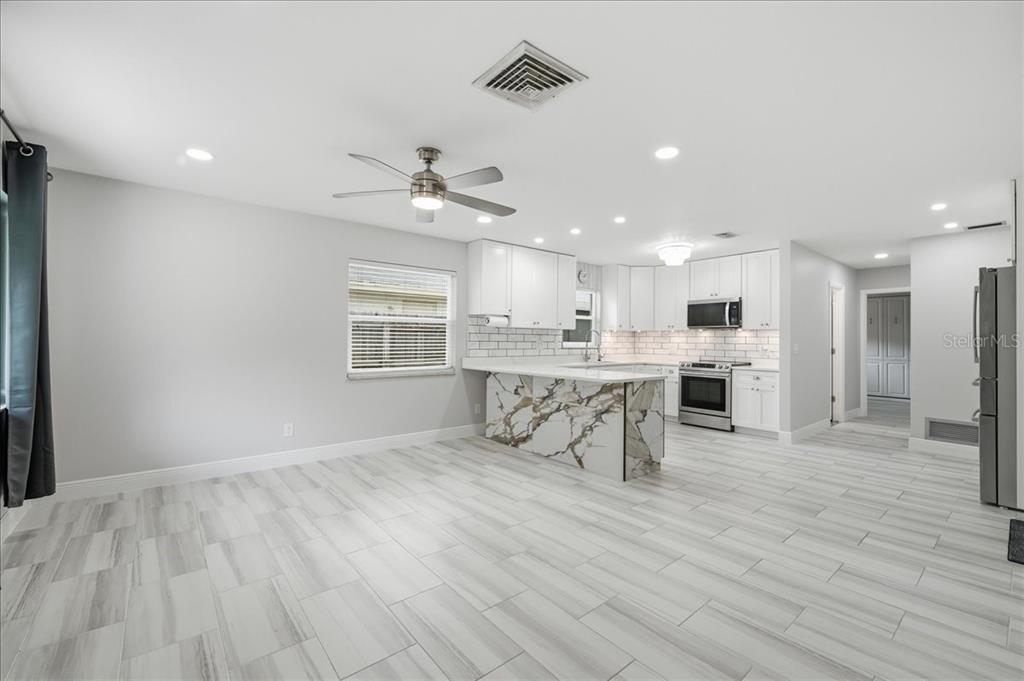 An open-concept kitchen and dining area with white cabinets, marble-patterned island, and light tile flooring — 311 45TH AVENUE N, ST PETERSBURG, FL