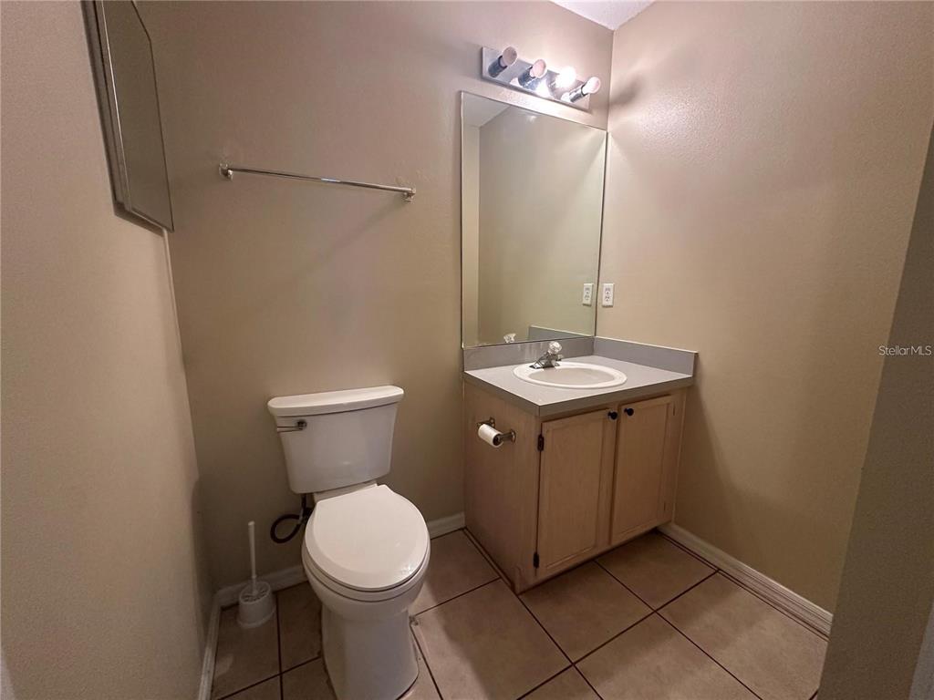 A bathroom features a toilet, a vanity with a sink, a mirror, and tiled flooring — 17432 WOODCREST WAY, CLERMONT, FL
