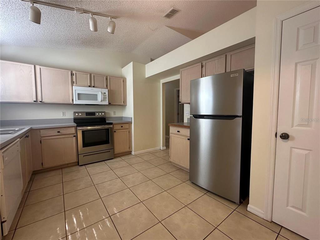 A kitchen features light wood cabinets, stainless steel appliances, and beige tile flooring — 17432 WOODCREST WAY, CLERMONT, FL
