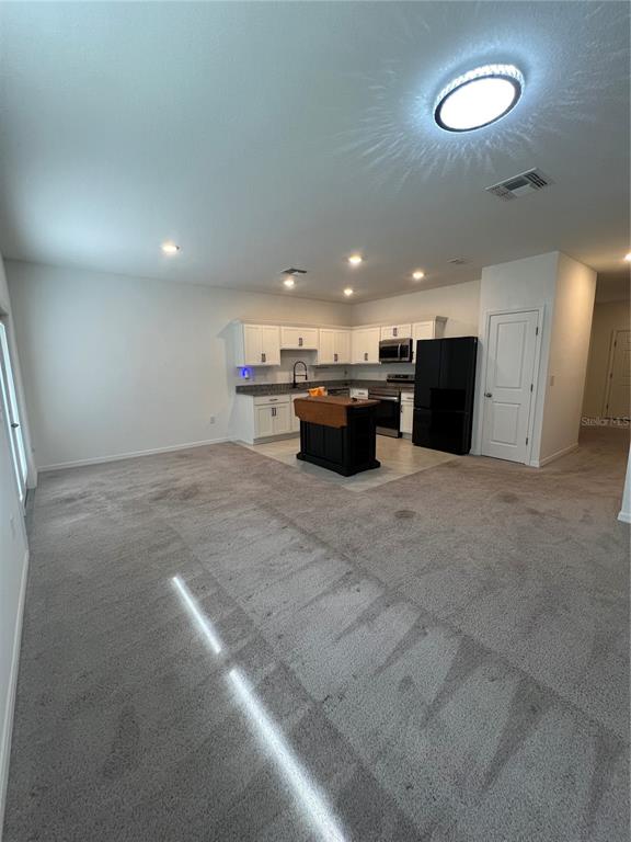 A kitchen with white cabinets and a dark island sits in a carpeted open room — 117 MANDOVI STREET, DAVENPORT, FL