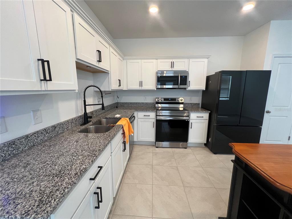 A kitchen features white cabinets, granite countertops, stainless steel appliances, and a black refrigerator — 117 MANDOVI STREET, DAVENPORT, FL