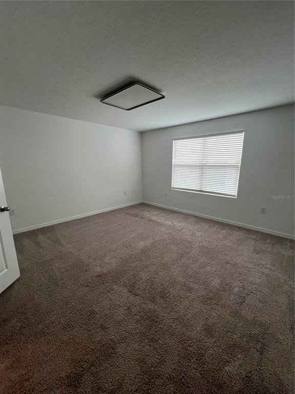 An empty bedroom features white walls, brown carpet, a window with blinds, and a ceiling light — 117 MANDOVI STREET, DAVENPORT, FL