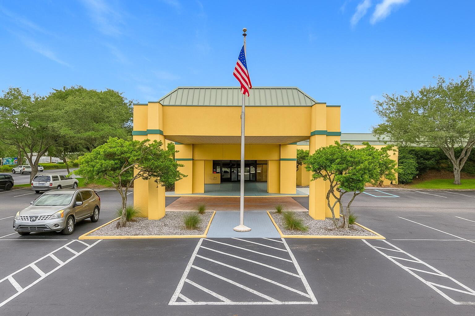 An exterior view of a yellow commercial building with a covered entrance and American flag — 910 Suemac Road, Jacksonville FL 32254, JACKSONVILLE, FL