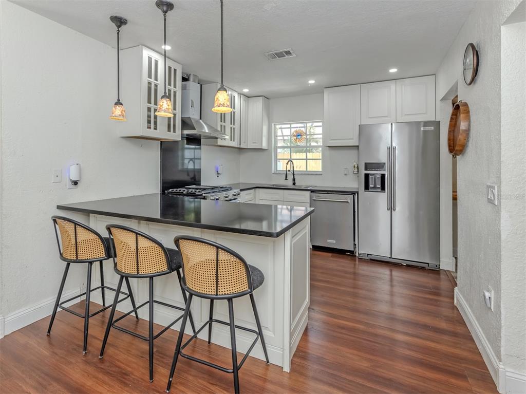 A kitchen features white cabinets, black countertops, stainless steel appliances, and three rattan bar stools — 1533 FUNDY ROAD, VENICE, FL