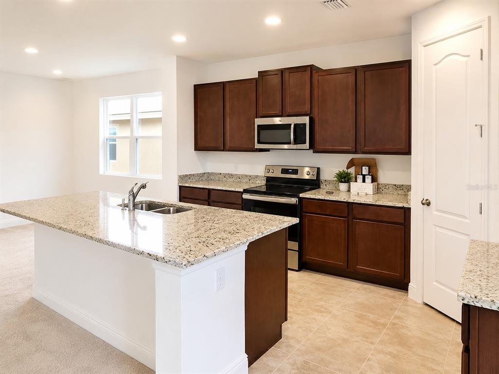 A kitchen features dark wood cabinets, granite countertops, a center island, and stainless steel appliances — 4932 OLIVIA COURT, ST CLOUD, FL