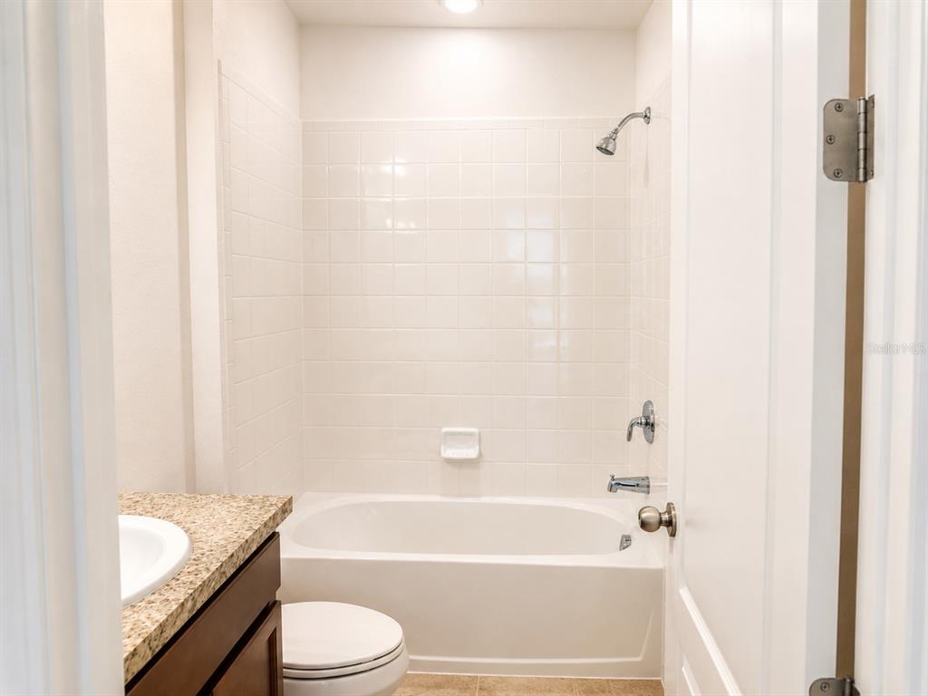 A bathroom features a white tiled shower-tub combination, a granite vanity, and a toilet — 4932 OLIVIA COURT, ST CLOUD, FL