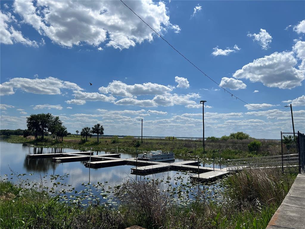 A wooden boat dock extends into a lake under a blue sky with scattered clouds — 901 AZALEA DRIVE, INDIAN LAKE ESTATES, FL
