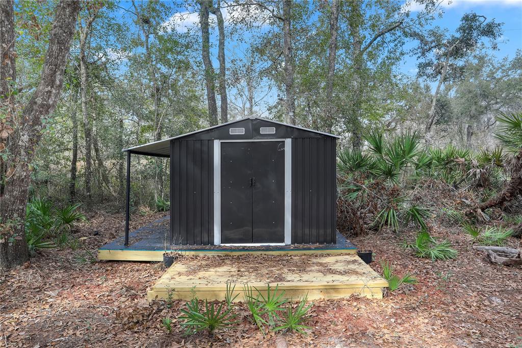 A dark metal storage shed sits on a wooden deck in a wooded area — 00 SE 929TH STREET, OLD TOWN, FL
