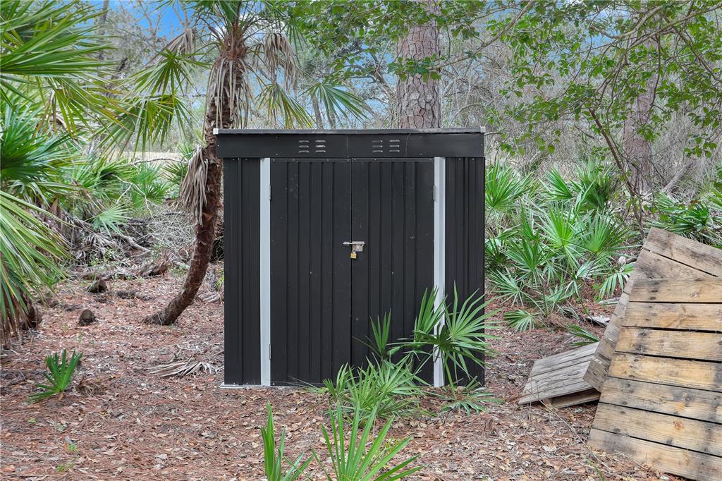 A black metal storage shed stands in a wooded area with palm trees and foliage — 00 SE 929TH STREET, OLD TOWN, FL