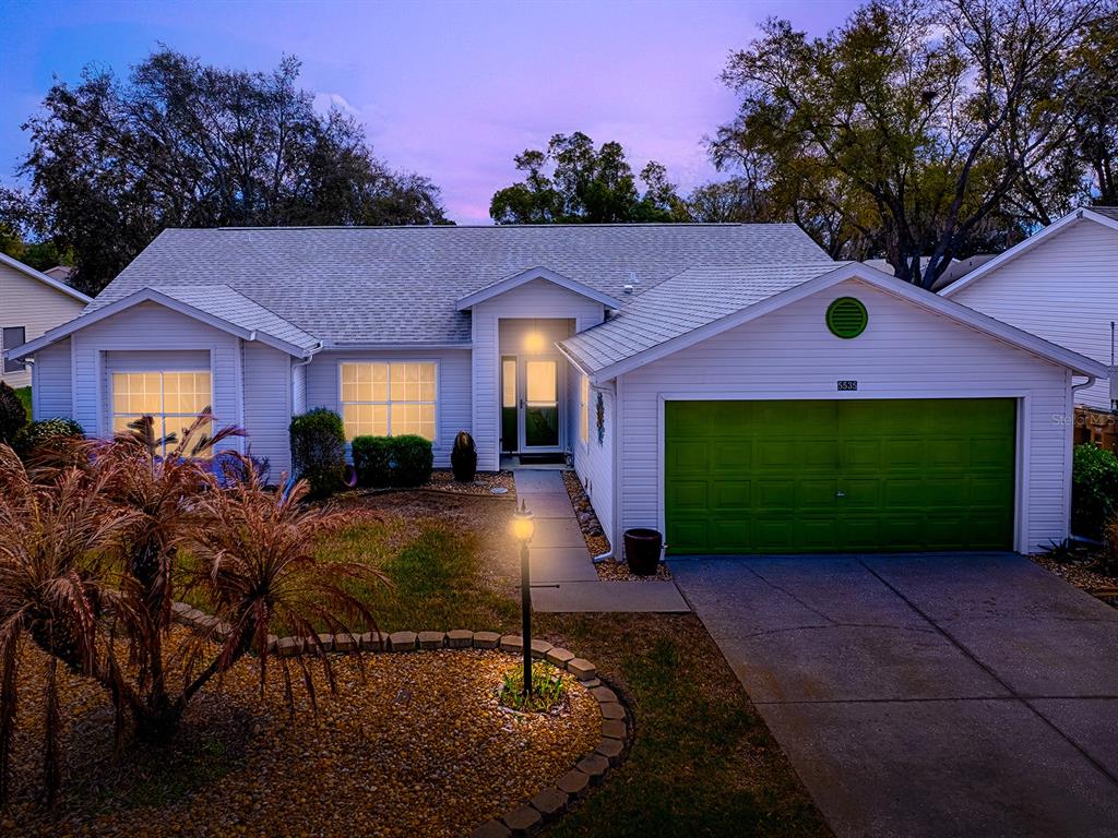 A single-story house with white siding, a green garage door, and a landscaped front yard — 5535 TANGELO STREET, LEESBURG, FL
