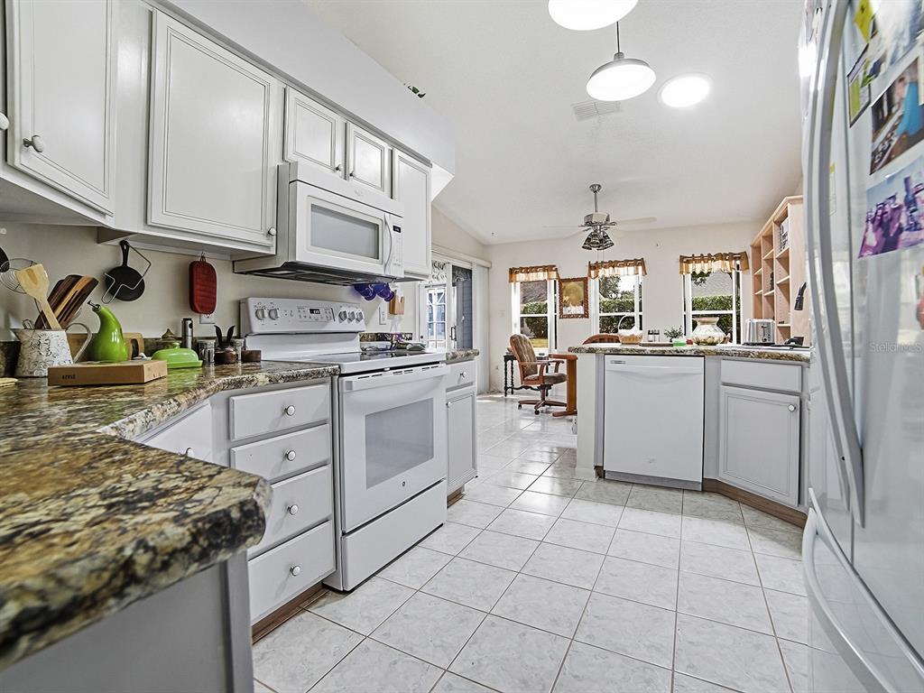 A kitchen with white cabinets, granite countertops, white appliances, and tiled flooring — 5535 TANGELO STREET, LEESBURG, FL