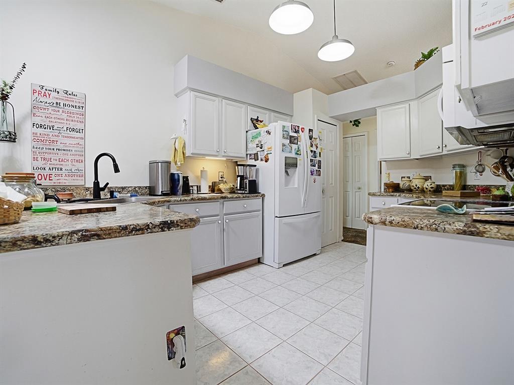 A kitchen features white cabinets, granite countertops, a white refrigerator, and light-colored tile flooring — 5535 TANGELO STREET, LEESBURG, FL