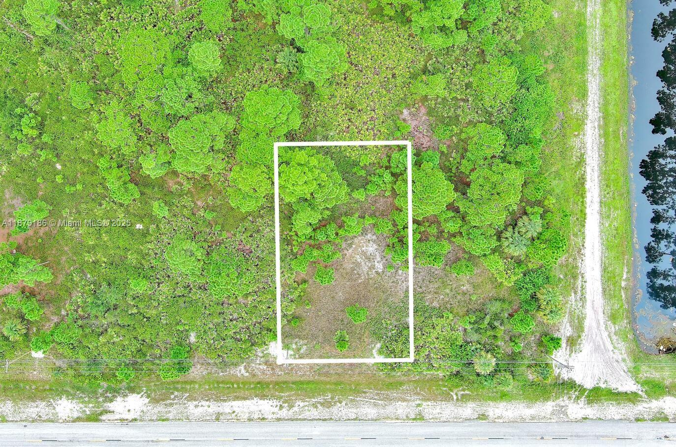 An aerial view shows a rectangular plot of land marked by a white outline — 702 Eisenhower Blvd, Lehigh Acres FL 33974, LEHIGH ACRES, FL