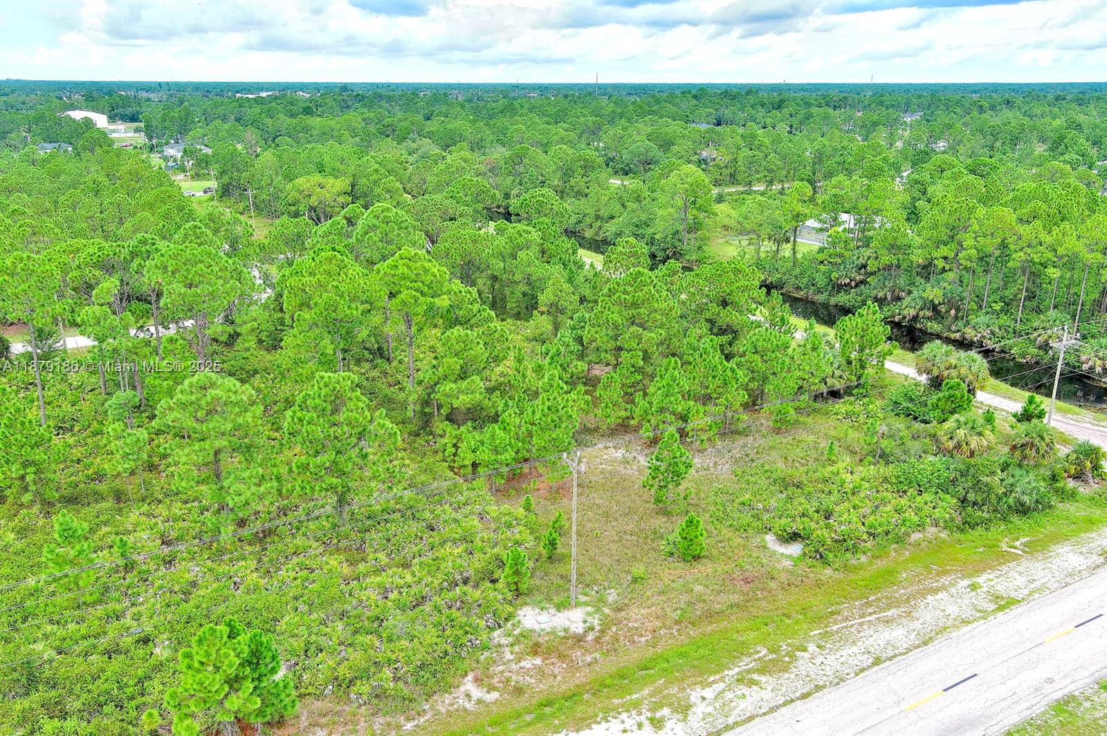 An aerial view shows a vacant, wooded lot bordering a canal and a paved road — 702 Eisenhower Blvd, Lehigh Acres FL 33974, LEHIGH ACRES, FL