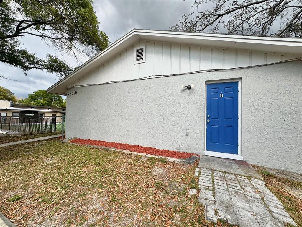A gray stucco building exterior features a blue door labeled B and a stone walkway — 10015 N ASTER AVENUE UNIT B, TAMPA, FL