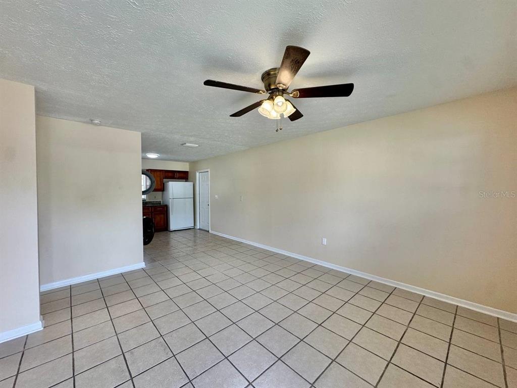 An open-concept room with light-colored tile flooring, a ceiling fan, and an adjacent kitchen — 10015 N ASTER AVENUE UNIT B, TAMPA, FL