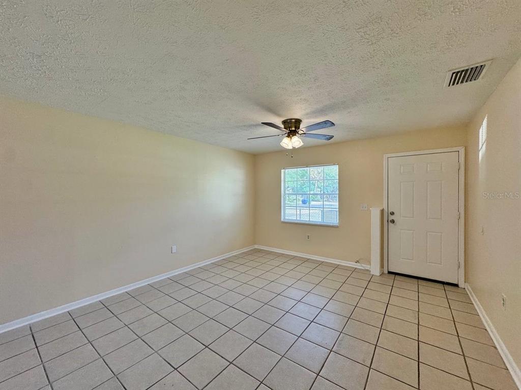 An empty room features beige walls, a tiled floor, a ceiling fan, and an exterior door — 10015 N ASTER AVENUE UNIT B, TAMPA, FL