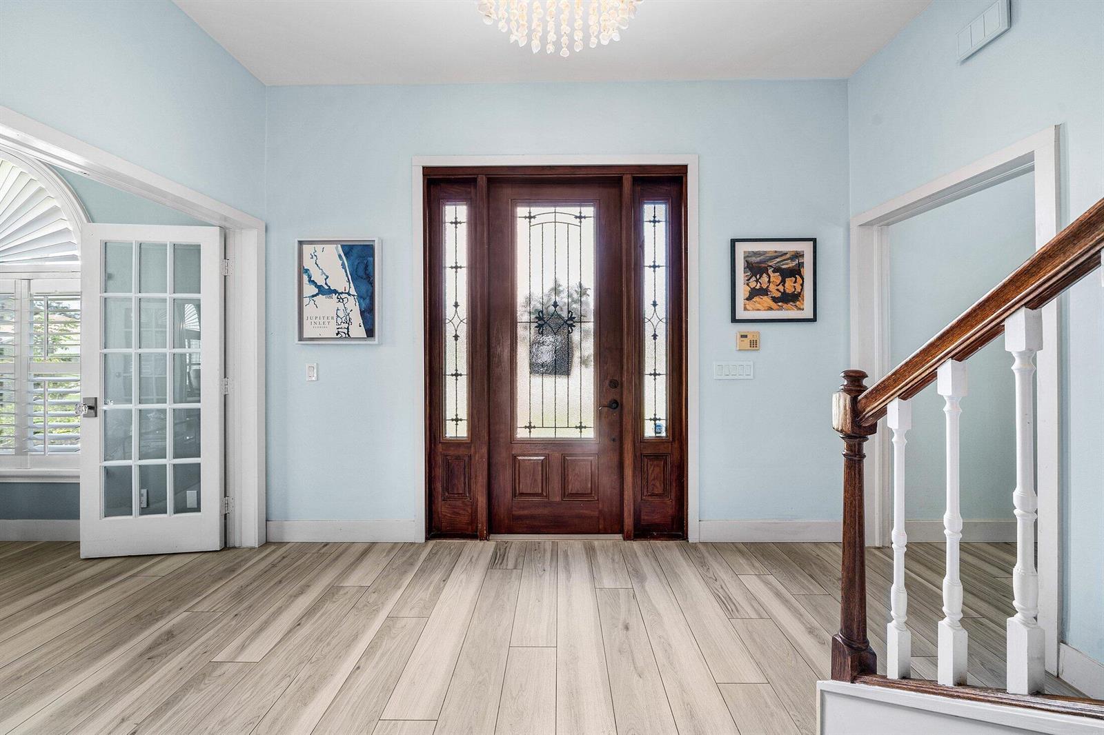 A bright entryway features light blue walls, wood-look flooring, a wooden front door, and a staircase — 208 Longshore Drive, Jupiter FL 33458, JUPITER, FL