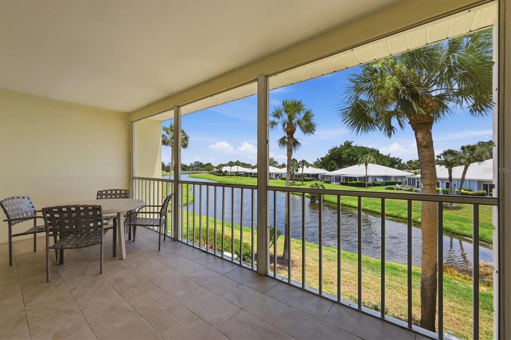 A screened-in balcony with tile flooring overlooks a canal and palm trees — 444 CERROMAR ROAD UNIT 298, VENICE, FL