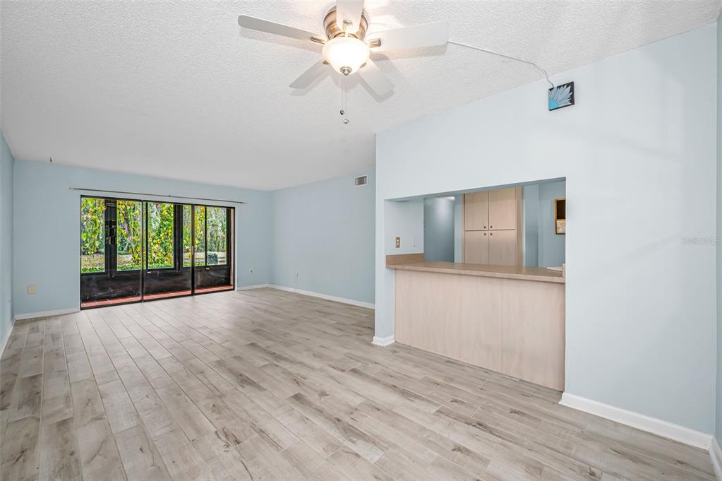 A living room with light blue walls, wood-look tile flooring, a ceiling fan, and a pass-through — 3232 LAKE PINE WAY E UNIT C1, TARPON SPRINGS, FL