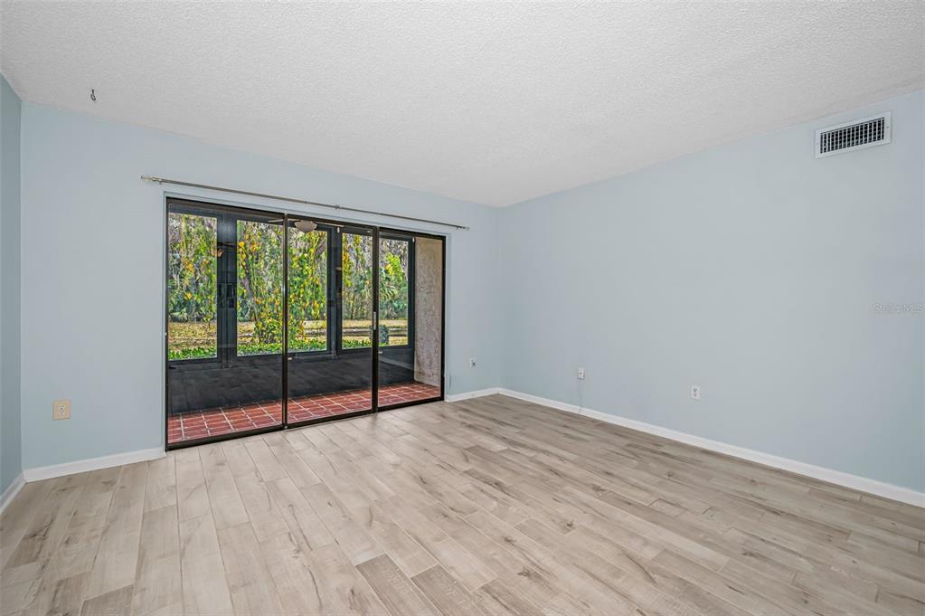 An empty room with light blue walls, wood-look flooring, and sliding glass doors to a patio — 3232 LAKE PINE WAY E UNIT C1, TARPON SPRINGS, FL