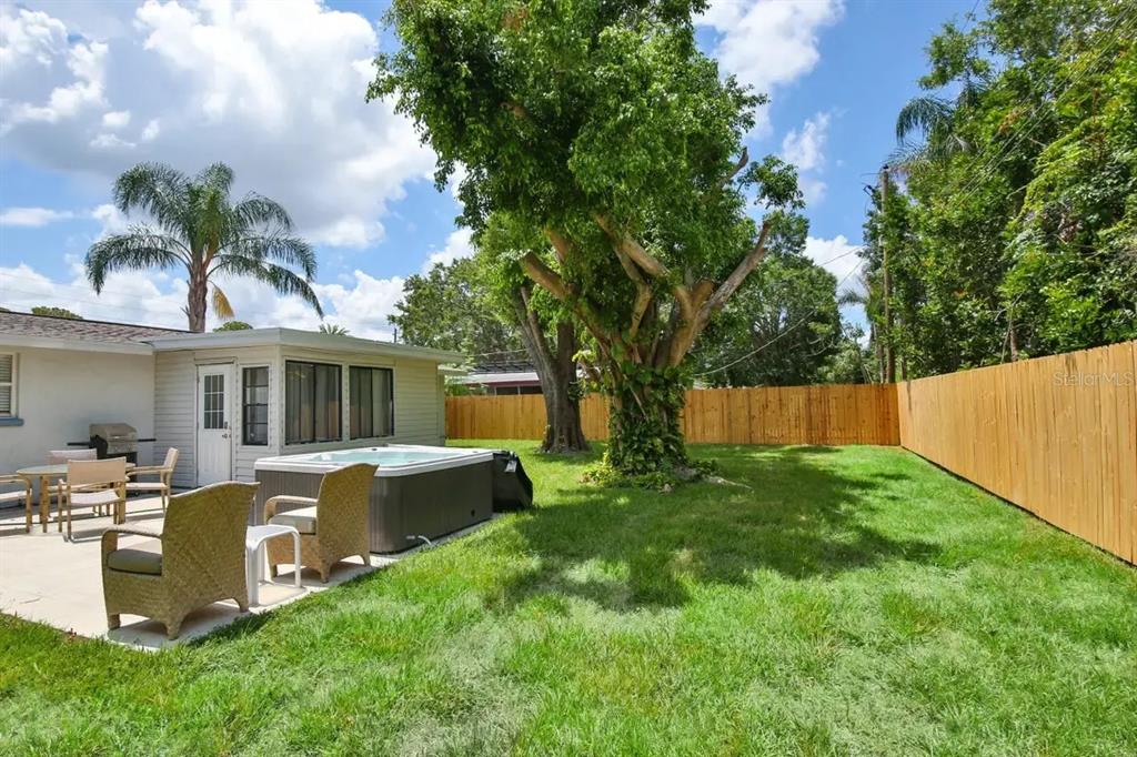 A backyard features a patio with a hot tub, wicker chairs, and a large tree — 5622 S LOCKWOOD RIDGE ROAD, SARASOTA, FL