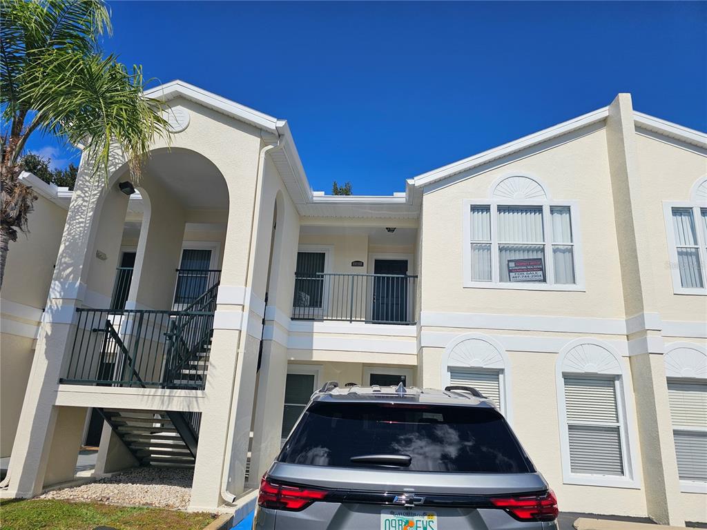 A two-story stucco apartment building features an exterior staircase and a parked silver SUV — 8815 GRAND PALMS CIRCLE UNIT B, KISSIMMEE, FL