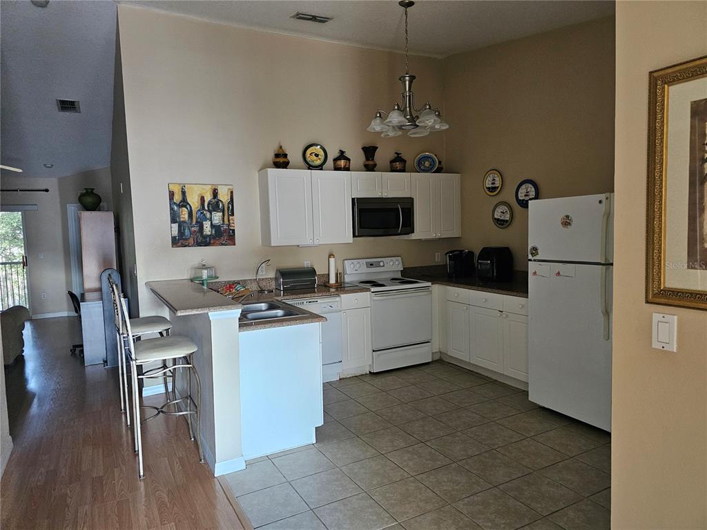 A kitchen features white cabinets, white appliances, a breakfast bar with stools, and tile flooring — 8815 GRAND PALMS CIRCLE UNIT B, KISSIMMEE, FL