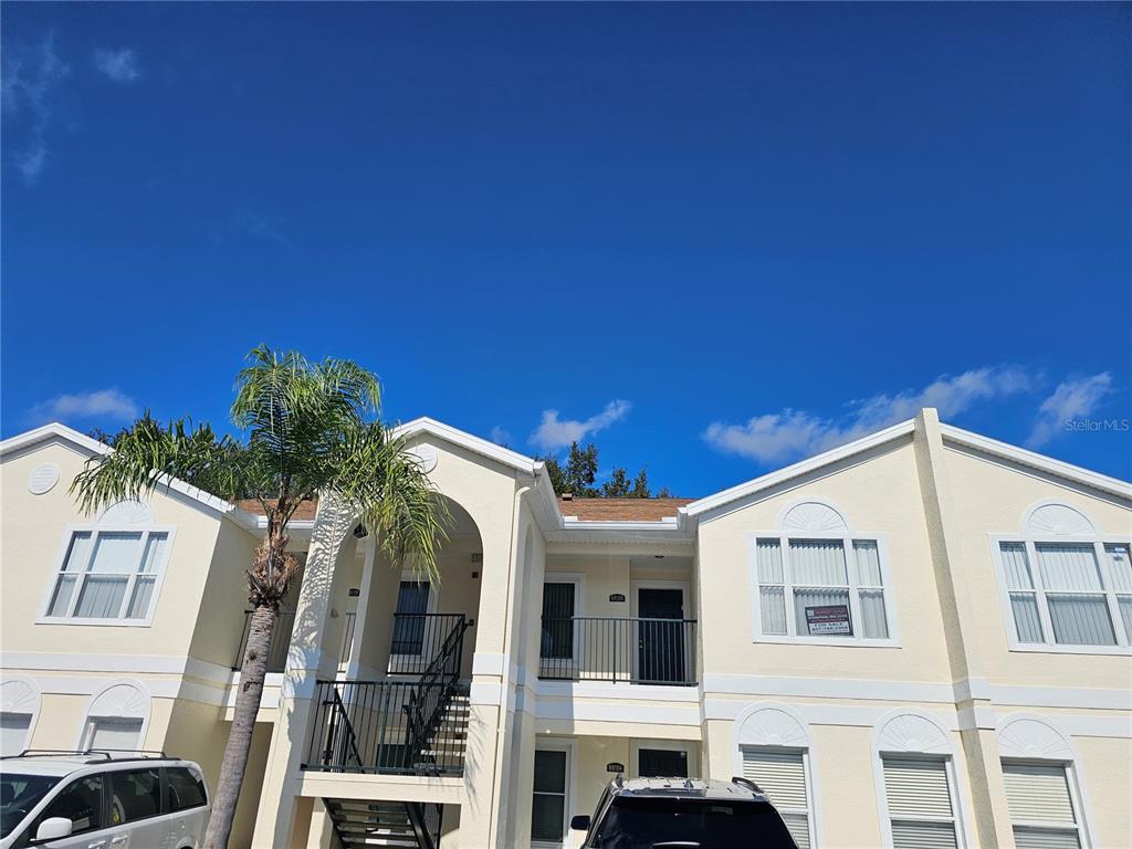 A two-story apartment building with light yellow stucco siding and a palm tree in front — 8815 GRAND PALMS CIRCLE UNIT B, KISSIMMEE, FL