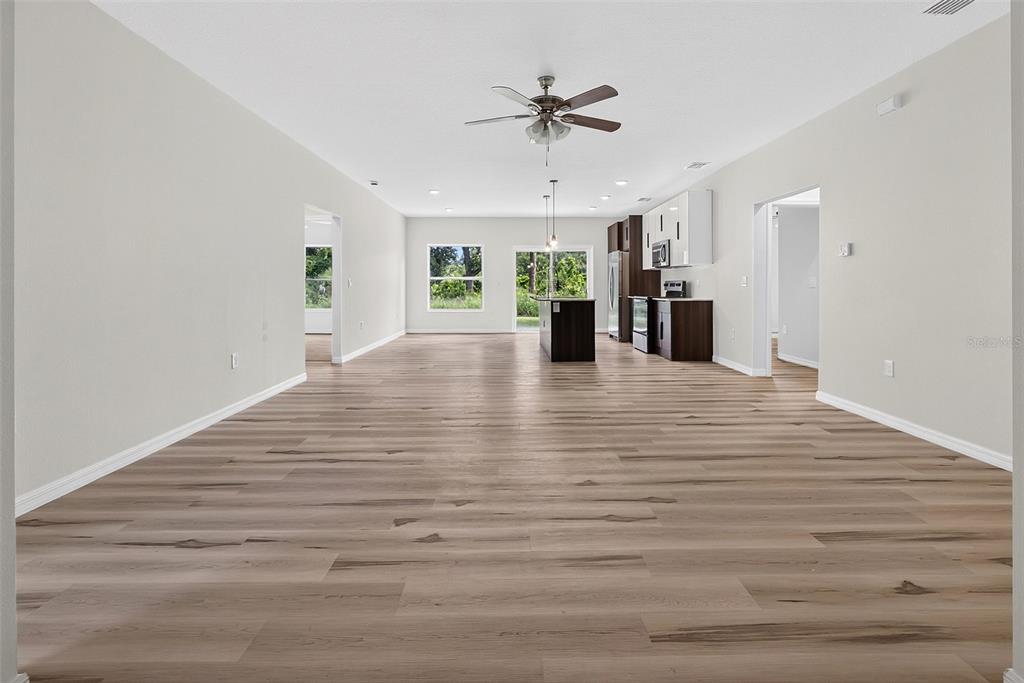 An open-concept living area features light wood-look flooring, white walls, and a modern kitchen — 14188 GABLES AVENUE, PORT CHARLOTTE, FL