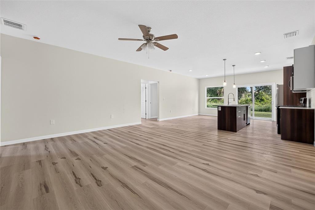 An open-concept living area features light wood-look flooring, a ceiling fan, and a kitchen island — 14188 GABLES AVENUE, PORT CHARLOTTE, FL
