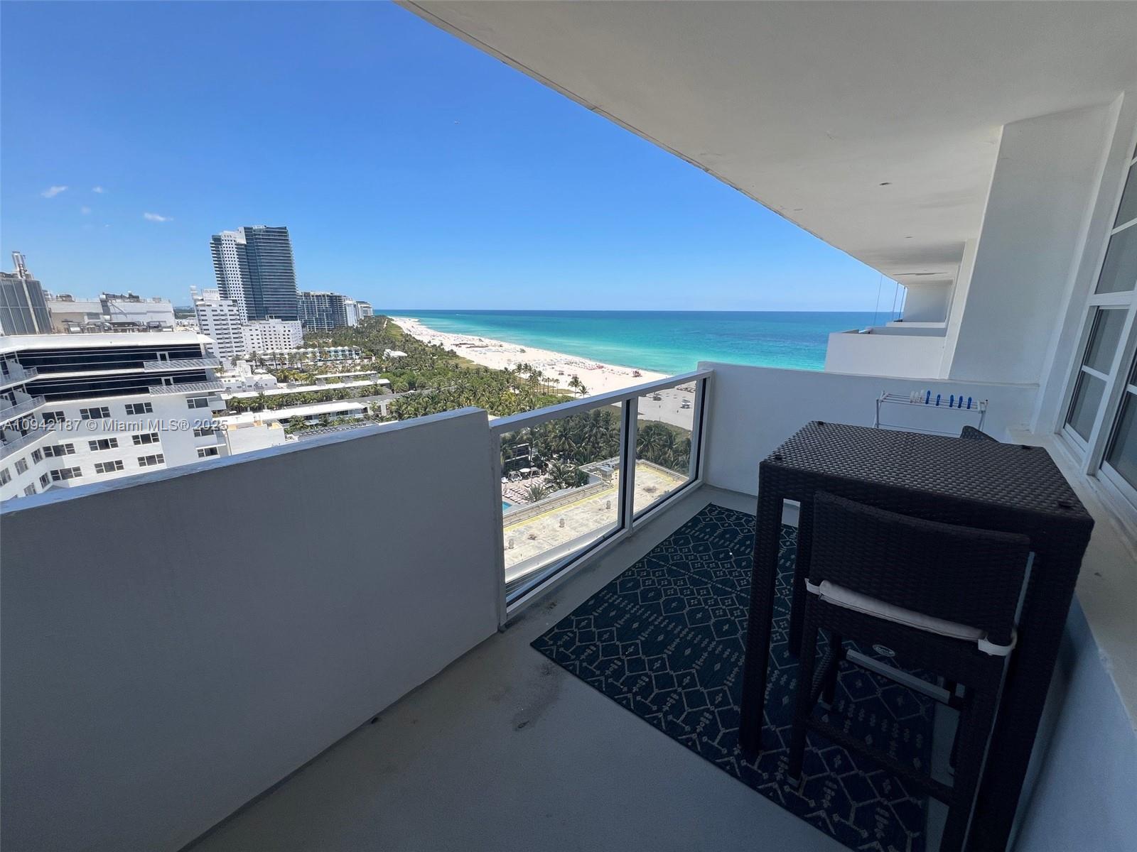 A balcony with a dark wicker table and chairs overlooks a beach and ocean — 100 Lincoln Rd # 1637, Miami Beach FL 33139, MIAMI BEACH, FL