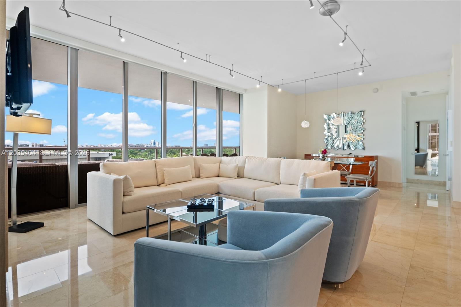 A modern living room features a large white sectional, blue armchairs, and floor-to-ceiling windows — 9705 Collins Ave # 605N, Bal Harbour FL 33154, BAL HARBOUR, FL
