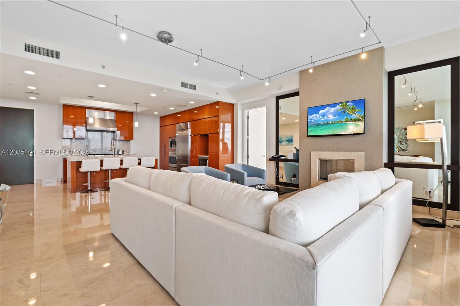 A modern living room features a white sectional sofa, a fireplace, and an open kitchen — 9705 Collins Ave # 605N, Bal Harbour FL 33154, BAL HARBOUR, FL