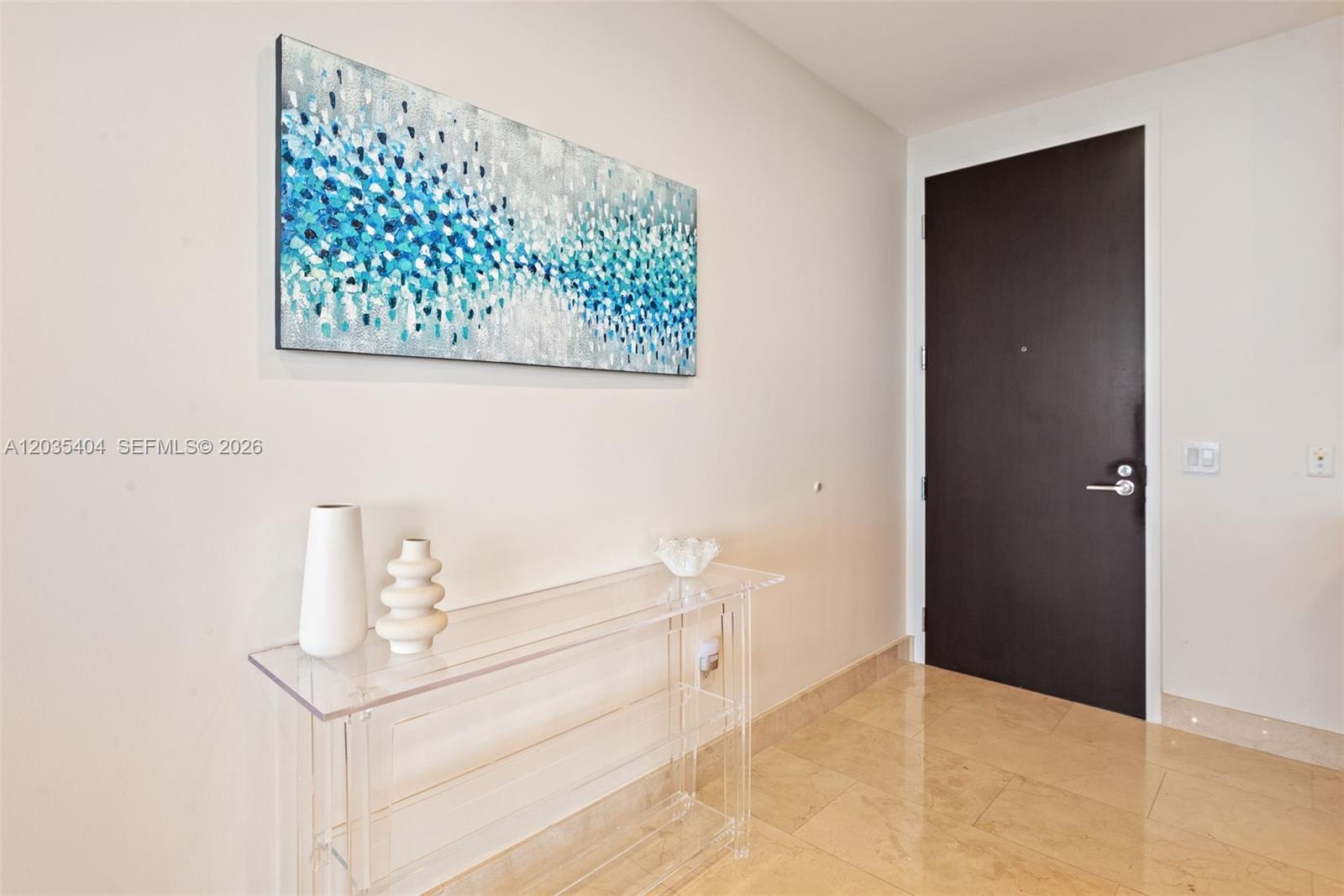 A modern entryway features a clear acrylic console table, abstract wall art, and tile flooring — 9705 Collins Ave # 605N, Bal Harbour FL 33154, BAL HARBOUR, FL