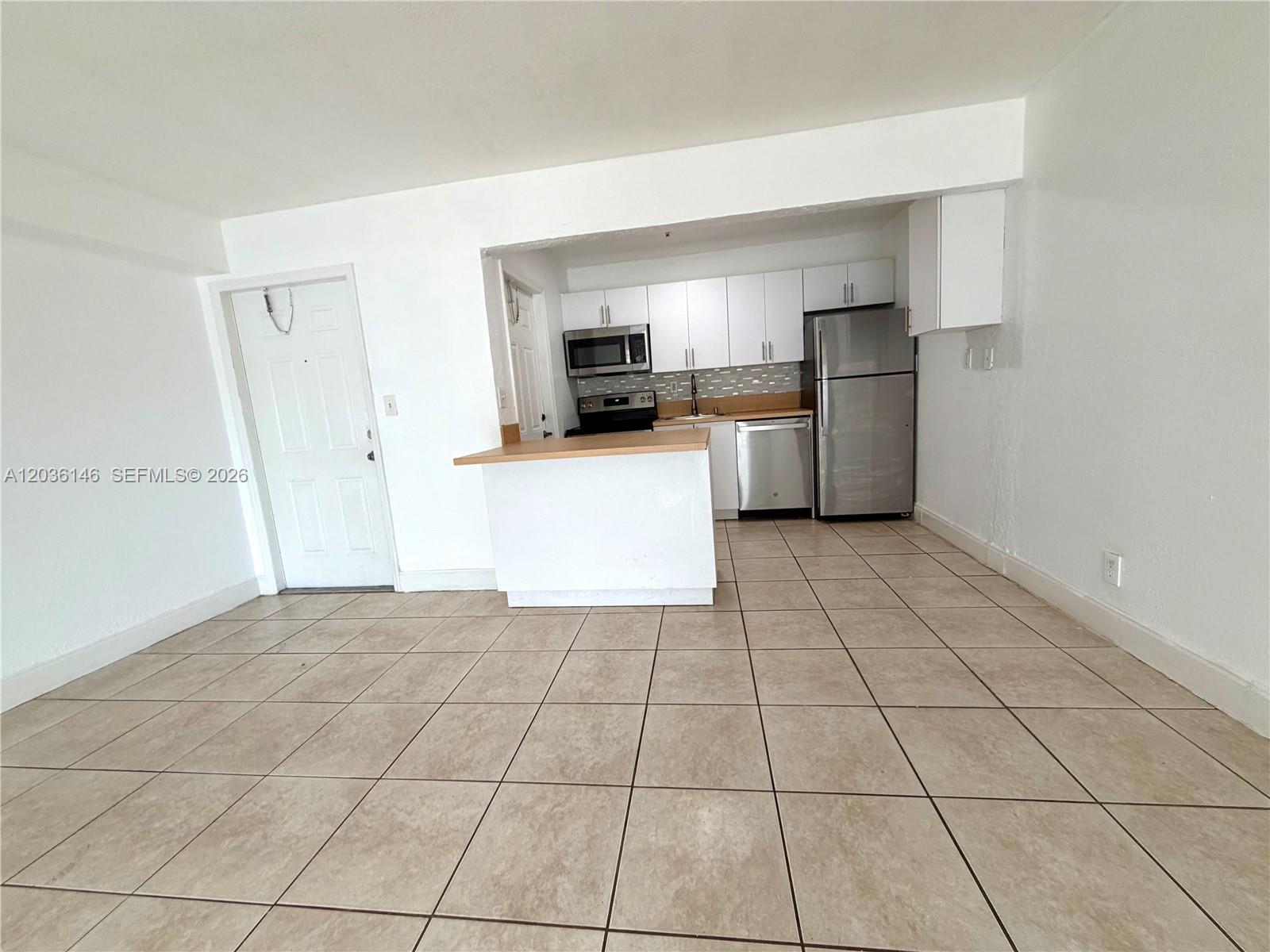 An open-concept kitchen with white cabinets and stainless steel appliances sits beside a tiled living area — 4271 NW 5th St # 128, Plantation FL 33317, PLANTATION, FL