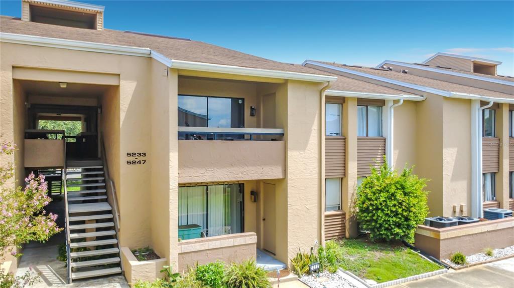 An exterior view of a two-story tan apartment building with an outdoor staircase — 5247 VINELAND ROAD UNIT 202, ORLANDO, FL