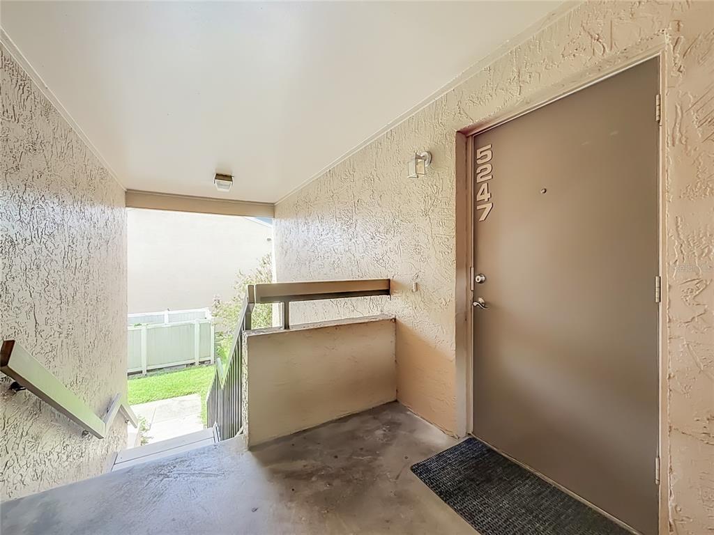An exterior view of a tan apartment door with the number 5247 and adjacent stairs — 5247 VINELAND ROAD UNIT 202, ORLANDO, FL