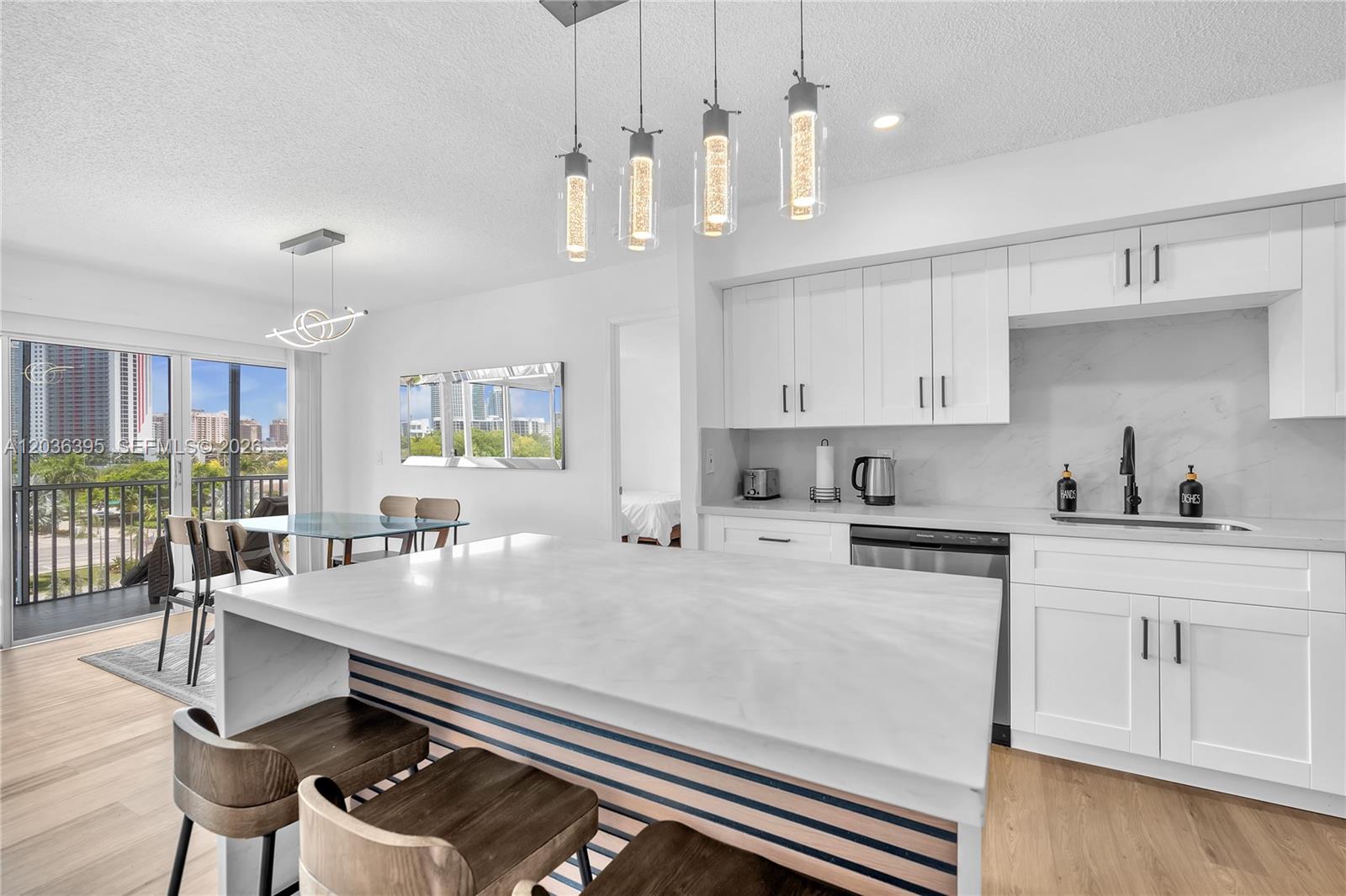 A modern kitchen features white cabinetry, a marble-topped island, and a view of city buildings — HALLANDALE BEACH, FL