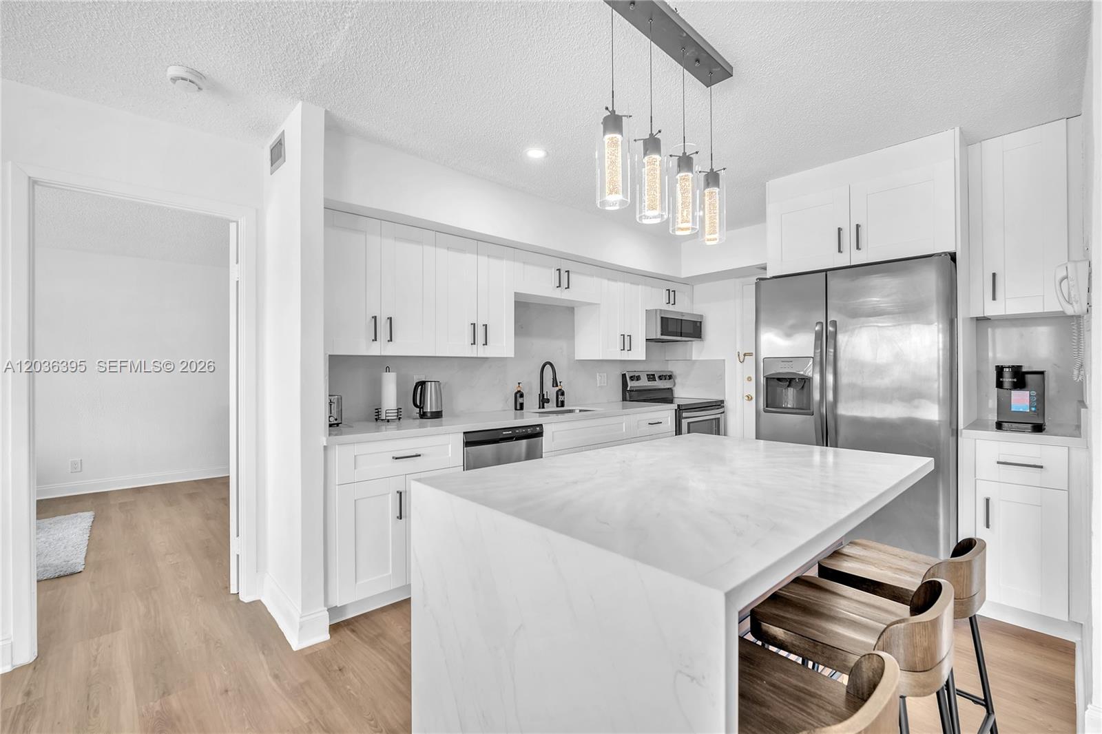 A modern kitchen features white cabinets, a marble-topped island, and stainless steel appliances — HALLANDALE BEACH, FL