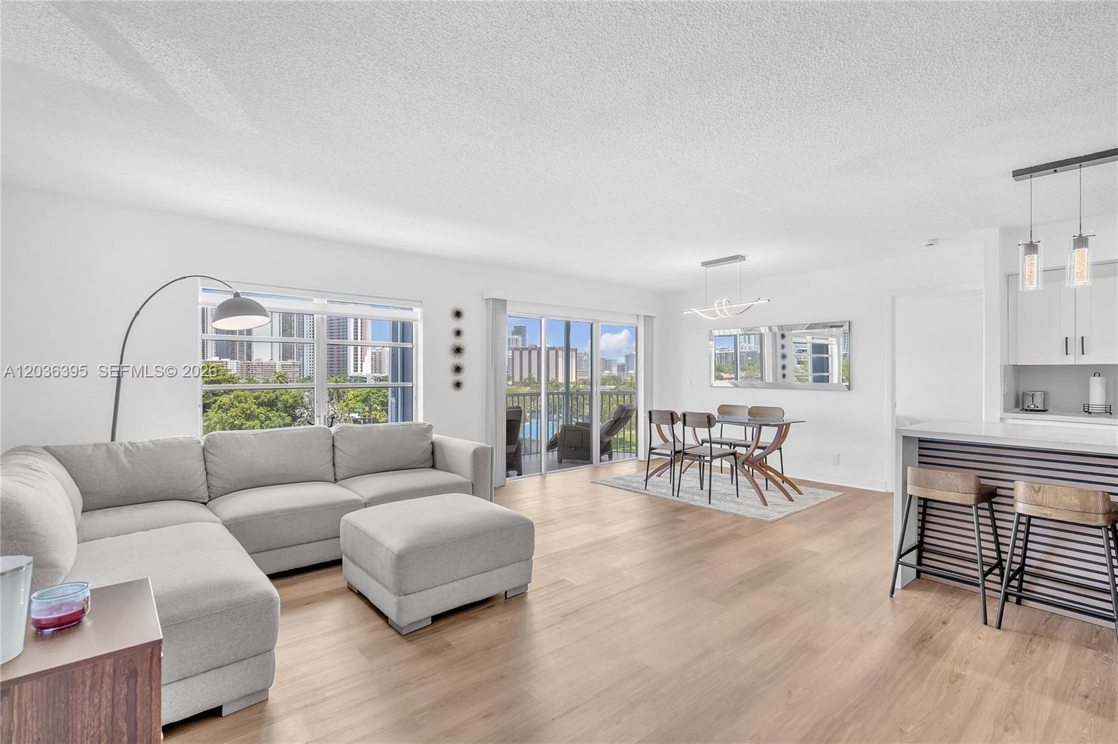 This open-concept living and dining area features light wood flooring, a sectional sofa, and balcony — HALLANDALE BEACH, FL
