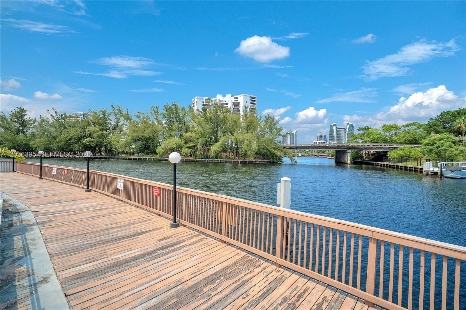 A wooden boardwalk overlooks a canal with a bridge and city buildings in the distance — HALLANDALE BEACH, FL