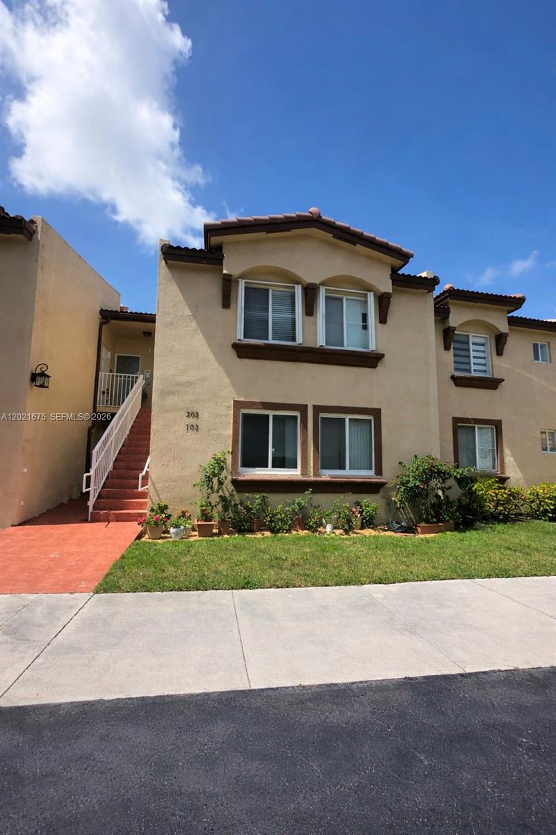 A two-story tan stucco apartment building features a red staircase and a small front garden — 15761 SW 137 ave # 202, Miami FL 33177, MIAMI, FL