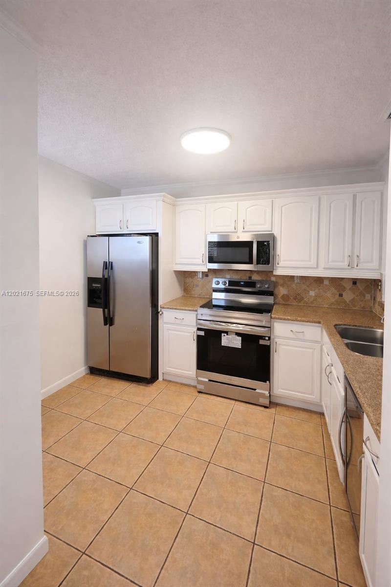 A kitchen features white cabinets, stainless steel appliances, tan countertops, and light-colored floor tiles — 15761 SW 137 ave # 202, Miami FL 33177, MIAMI, FL