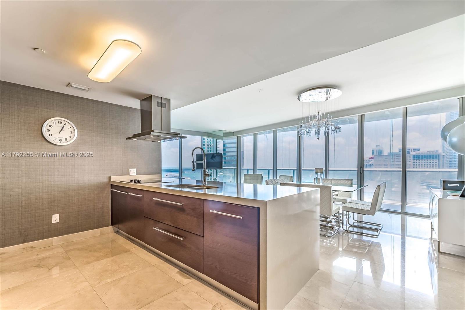 A modern kitchen features dark wood cabinetry, a waterfall island, and floor-to-ceiling windows with views — 495 Brickell Ave # 2801, Miami FL 33131, MIAMI, FL