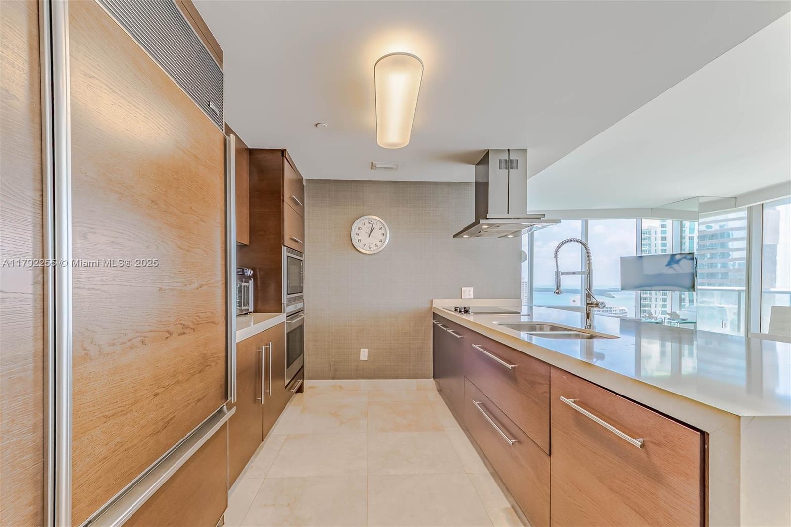 A modern kitchen features wood-toned cabinetry, stainless steel appliances, and a view of the ocean — 495 Brickell Ave # 2801, Miami FL 33131, MIAMI, FL