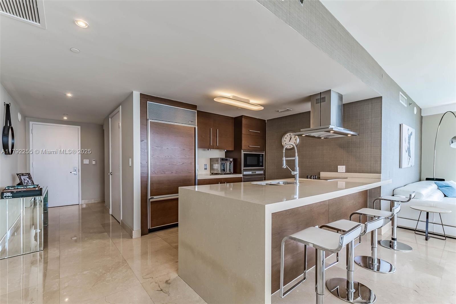 A modern kitchen features a large quartz island, wood cabinetry, and stainless steel appliances — 495 Brickell Ave # 2801, Miami FL 33131, MIAMI, FL